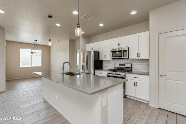 kitchen featuring sink, appliances with stainless steel finishes, an island with sink, white cabinets, and decorative light fixtures