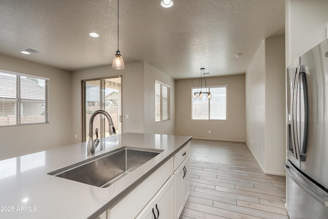 kitchen with stainless steel refrigerator with ice dispenser, decorative light fixtures, sink, and white cabinets