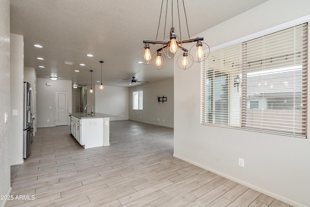 kitchen featuring pendant lighting, sink, stainless steel refrigerator, white cabinetry, and a center island with sink