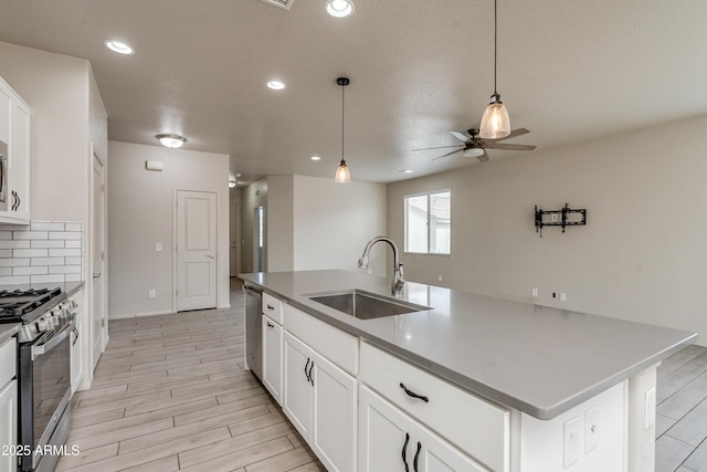 kitchen with sink, appliances with stainless steel finishes, white cabinets, and a center island with sink