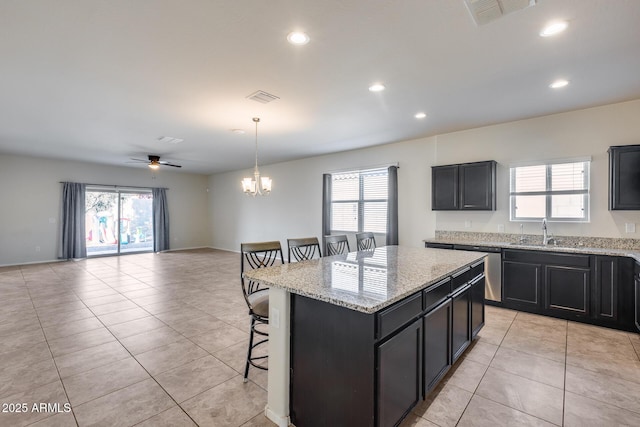 kitchen with light tile patterned flooring, a kitchen island, sink, a breakfast bar area, and hanging light fixtures