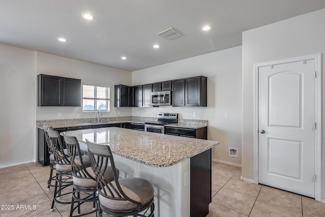 kitchen featuring a kitchen island, appliances with stainless steel finishes, sink, a kitchen breakfast bar, and light stone countertops