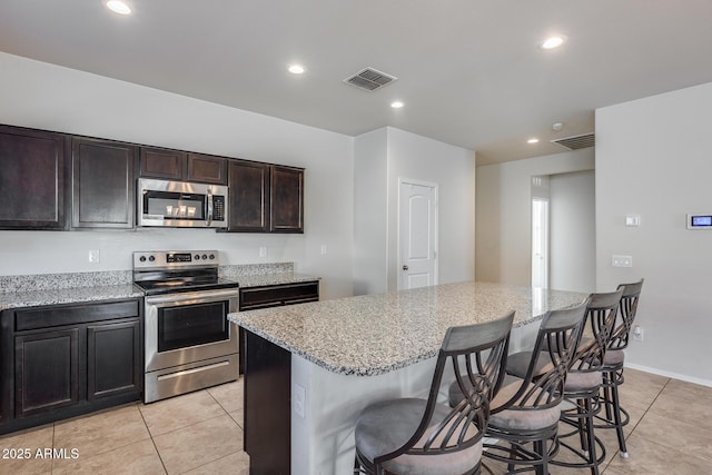 kitchen featuring a breakfast bar area, a center island, dark brown cabinets, appliances with stainless steel finishes, and light stone countertops