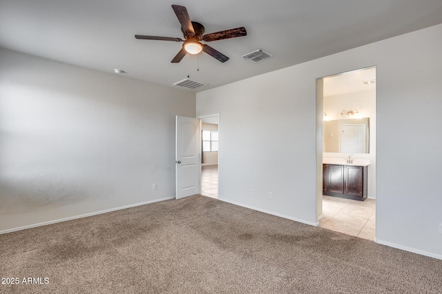 unfurnished bedroom featuring ceiling fan, light colored carpet, sink, and ensuite bath