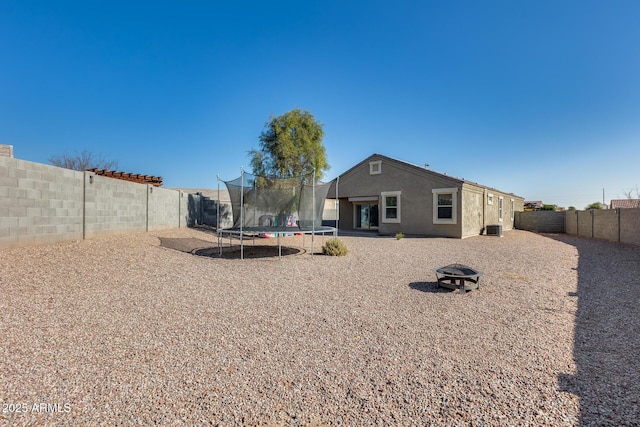 back of house featuring a trampoline, cooling unit, and an outdoor fire pit