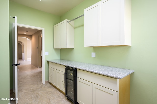 kitchen with white cabinetry, light stone counters, and beverage cooler