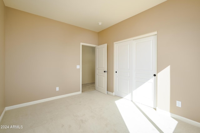 unfurnished bedroom with baseboards, light carpet, and a closet