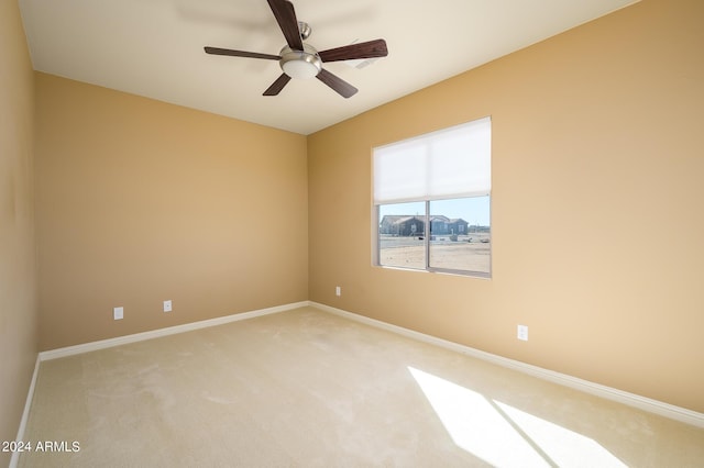 spare room with light colored carpet, a ceiling fan, and baseboards