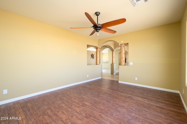 empty room featuring visible vents, a ceiling fan, baseboards, dark wood-style floors, and arched walkways