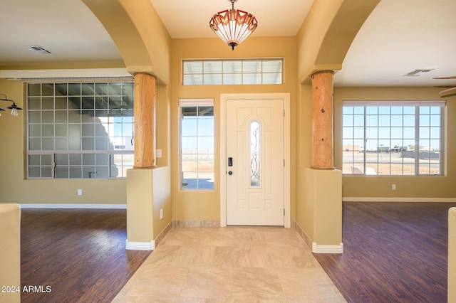 entrance foyer featuring arched walkways, decorative columns, wood finished floors, and visible vents