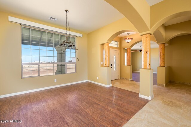 unfurnished room with decorative columns, visible vents, arched walkways, wood finished floors, and a notable chandelier