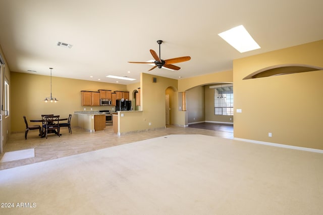 unfurnished living room with light colored carpet, arched walkways, a ceiling fan, baseboards, and visible vents