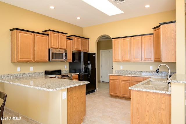 kitchen featuring arched walkways, a sink, light stone counters, a peninsula, and stainless steel appliances