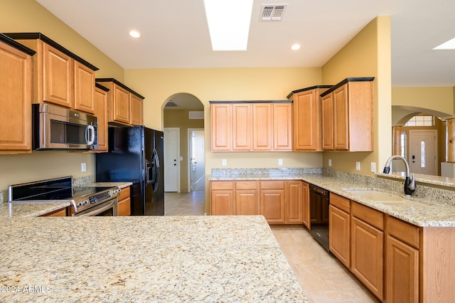 kitchen featuring kitchen peninsula, light stone countertops, black appliances, and sink