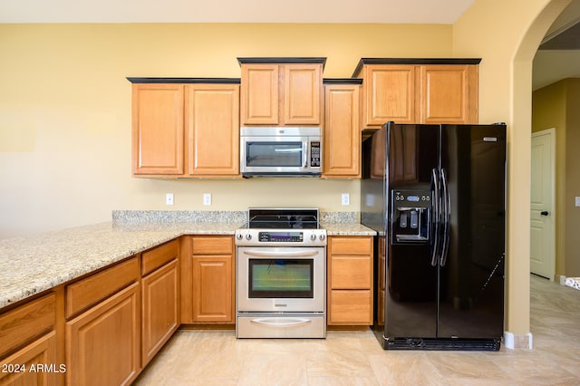kitchen featuring arched walkways, appliances with stainless steel finishes, and light stone counters