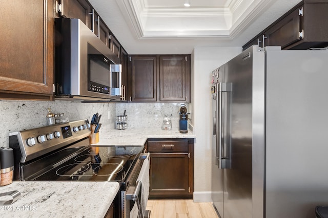 kitchen with ornamental molding, a raised ceiling, stainless steel appliances, light stone countertops, and backsplash