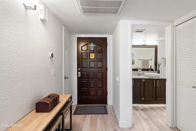 foyer entrance with light hardwood / wood-style floors, sink, and a textured ceiling