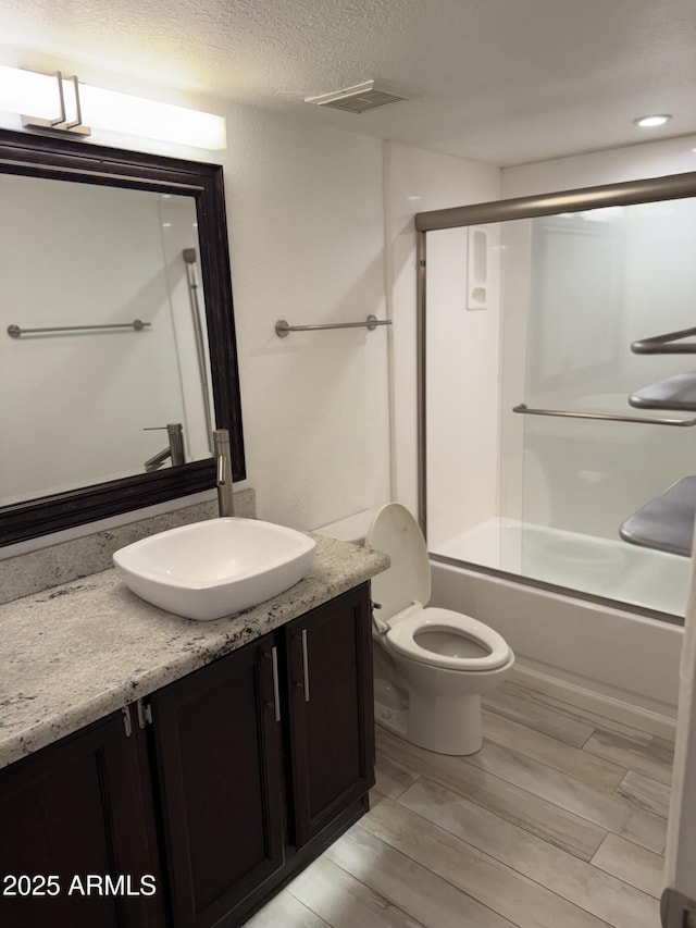 full bathroom featuring vanity, combined bath / shower with glass door, a textured ceiling, and toilet