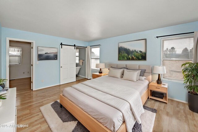 bedroom with baseboards, a barn door, and light wood-style floors