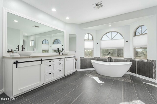 4497 E Carriage Way, Gilbert, AZ 85297 - bathroom with a wainscoted wall, double vanity, a freestanding tub, recessed lighting, and tile walls