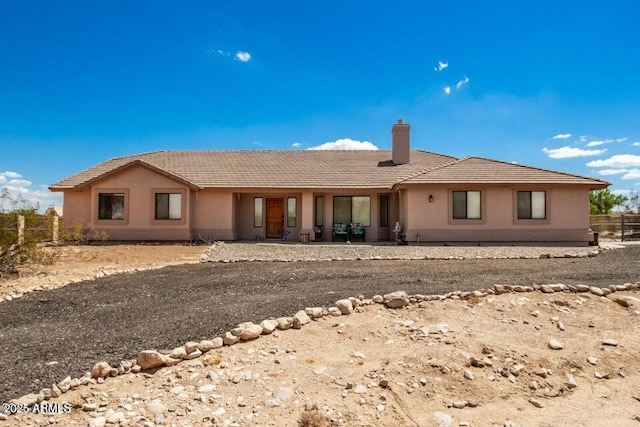 back of house featuring stucco siding, fence, a tiled roof, and a chimney