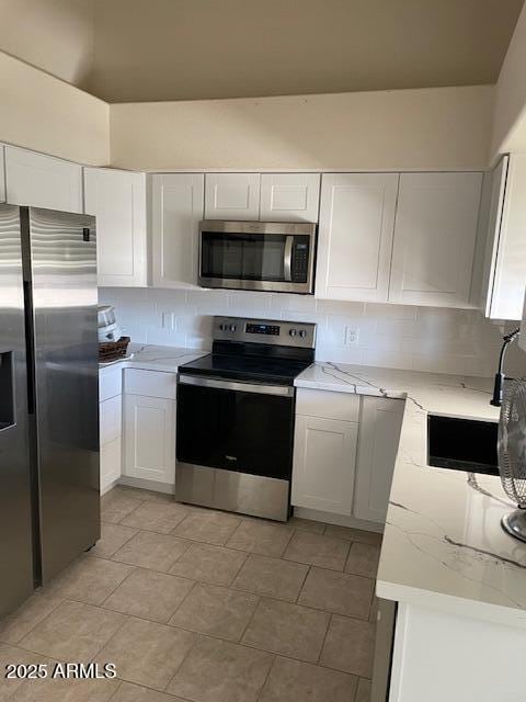 kitchen with white cabinets, stainless steel appliances, light stone counters, and decorative backsplash