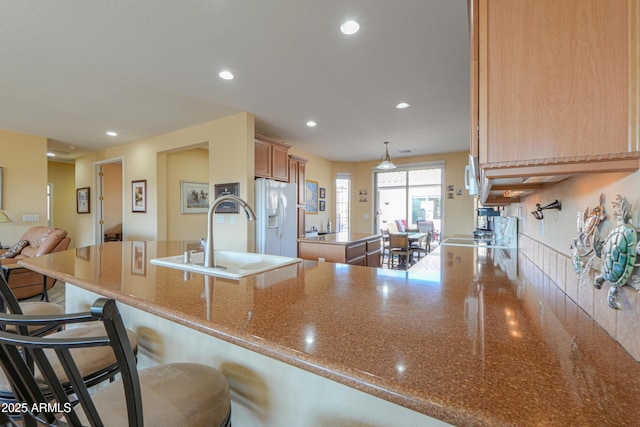 kitchen with sink, a breakfast bar, white refrigerator with ice dispenser, decorative light fixtures, and kitchen peninsula