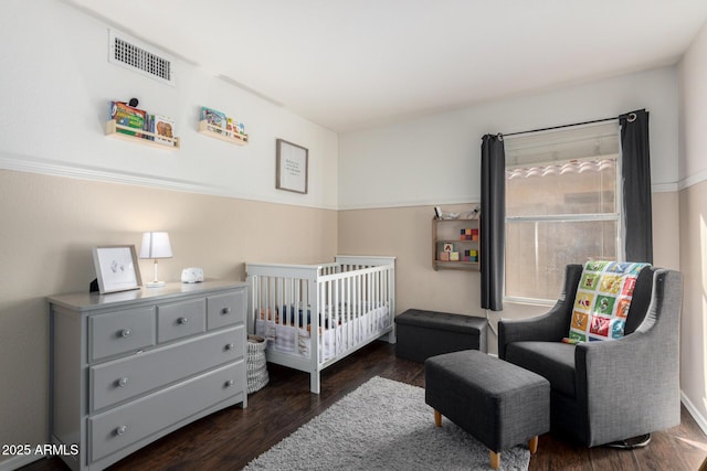 bedroom featuring dark wood-style floors, visible vents, and a crib