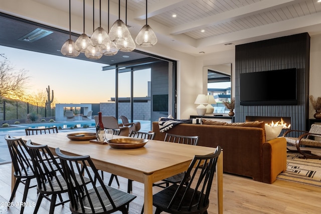 dining space featuring light wood-type flooring, beam ceiling, a lit fireplace, and recessed lighting