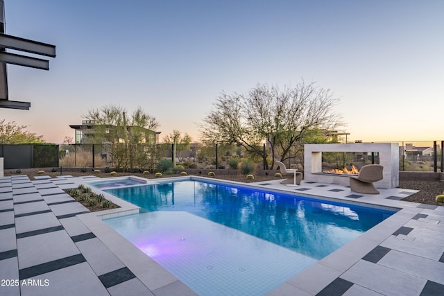 pool at dusk with a fenced in pool, a patio, a multi sided fireplace, and fence