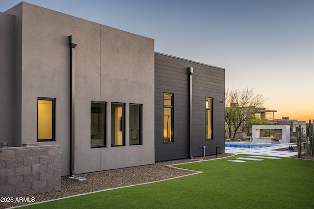 back of property at dusk featuring an outdoor pool, a lawn, and stucco siding