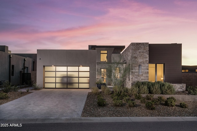 contemporary home with a garage, stone siding, decorative driveway, and stucco siding