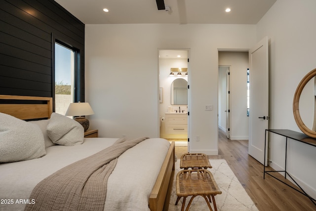 bedroom with baseboards, light wood-style flooring, ensuite bathroom, a sink, and recessed lighting