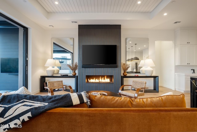 living room featuring a tray ceiling, a large fireplace, visible vents, and recessed lighting