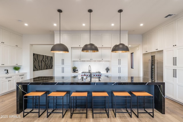 kitchen with a breakfast bar, a sink, visible vents, white cabinetry, and light wood-style floors