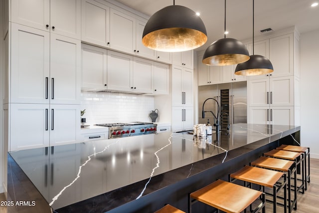 kitchen with visible vents, light wood-style flooring, a sink, white cabinetry, and backsplash