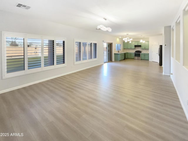 unfurnished living room with a healthy amount of sunlight, a chandelier, sink, and light wood-type flooring