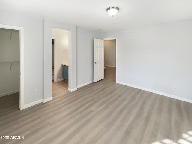 unfurnished bedroom featuring a walk in closet, light hardwood / wood-style floors, a closet, and ensuite bathroom