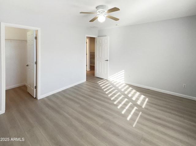 unfurnished bedroom with hardwood / wood-style flooring, a walk in closet, a closet, and ceiling fan