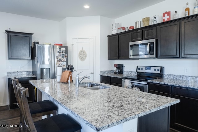 kitchen featuring a kitchen island with sink, sink, light stone counters, and appliances with stainless steel finishes