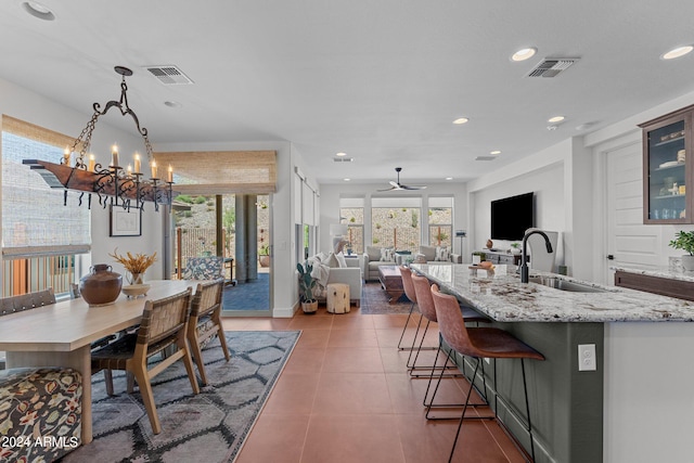 kitchen featuring sink, hanging light fixtures, a kitchen island with sink, light stone countertops, and ceiling fan with notable chandelier