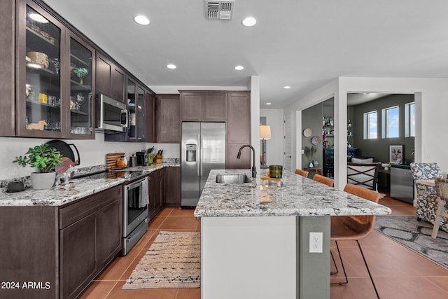 kitchen with a kitchen bar, sink, appliances with stainless steel finishes, light tile patterned floors, and dark brown cabinets