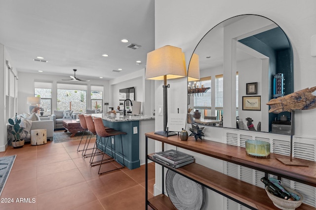 kitchen featuring ceiling fan, a kitchen breakfast bar, light tile patterned flooring, light stone countertops, and sink