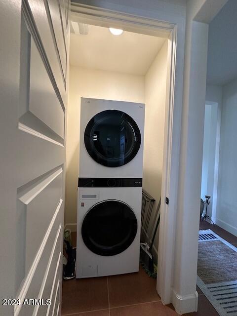 laundry area featuring dark tile patterned flooring and stacked washer / drying machine