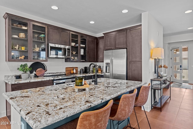 kitchen with light stone countertops, stainless steel appliances, a kitchen island with sink, and tile patterned flooring