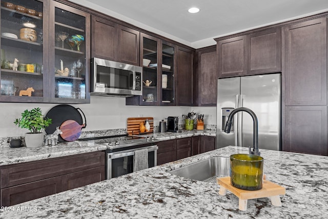 kitchen featuring light stone countertops, appliances with stainless steel finishes, sink, and dark brown cabinetry