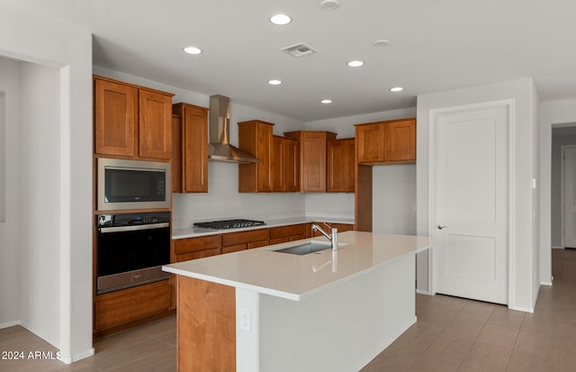 kitchen featuring wall chimney range hood, a center island with sink, light tile patterned floors, sink, and stainless steel appliances