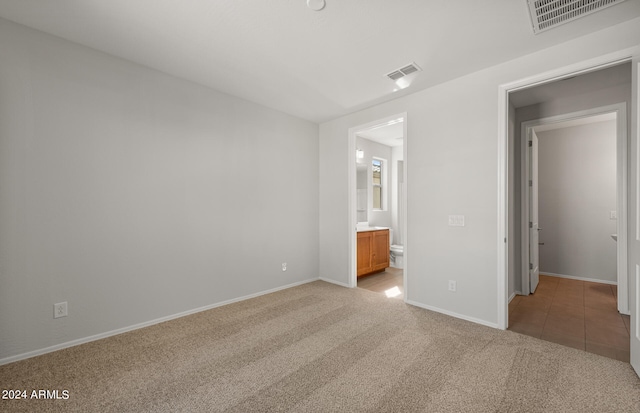 unfurnished bedroom with connected bathroom and light colored carpet