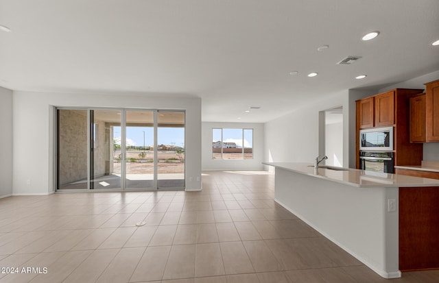 kitchen with light tile patterned floors, stainless steel appliances, sink, and a kitchen island with sink