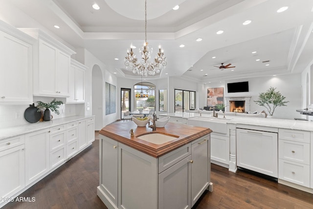 kitchen featuring a raised ceiling, a kitchen island, ceiling fan with notable chandelier, white cabinets, and dishwashing machine